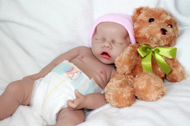 Infant doll lying on a blanket alongside a plush teddy bear.